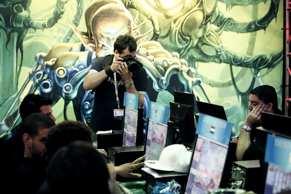 Players competing at a large Magic: The Gathering tournament in front of a giant card-art mural